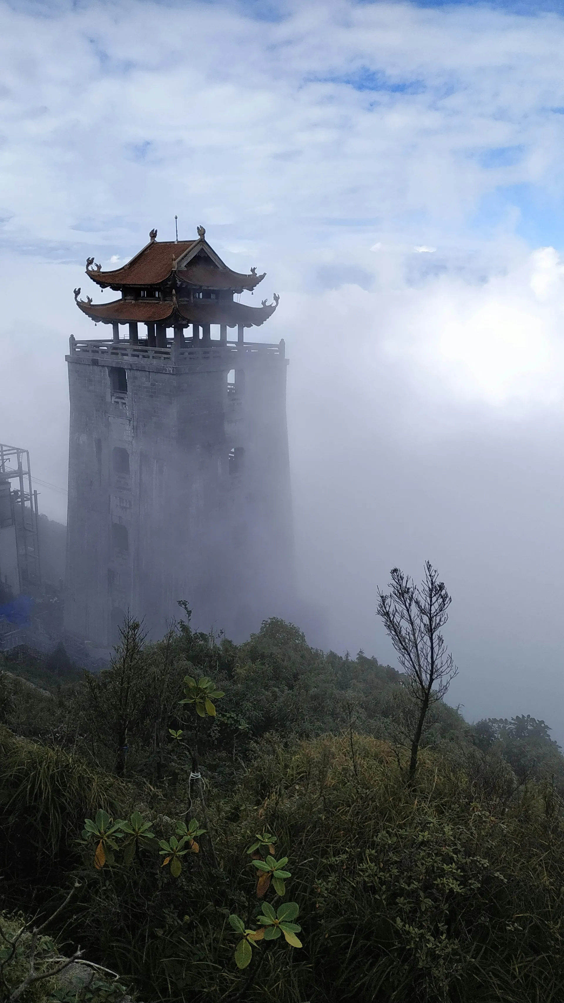A traditional mountain pavilion partly hidden by mist and pale clouds
