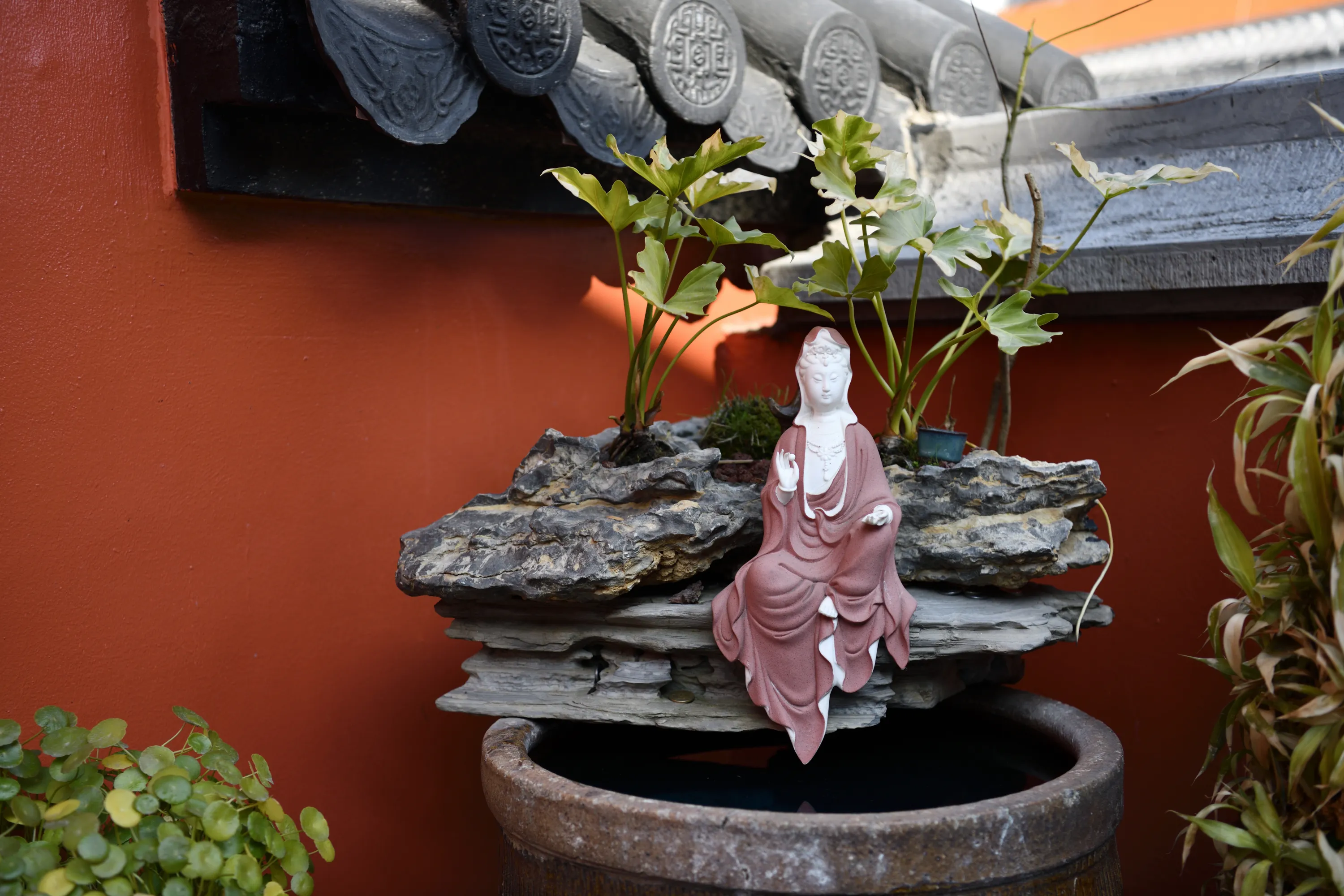 Temple roof tiles above green leaves and a quiet courtyard object