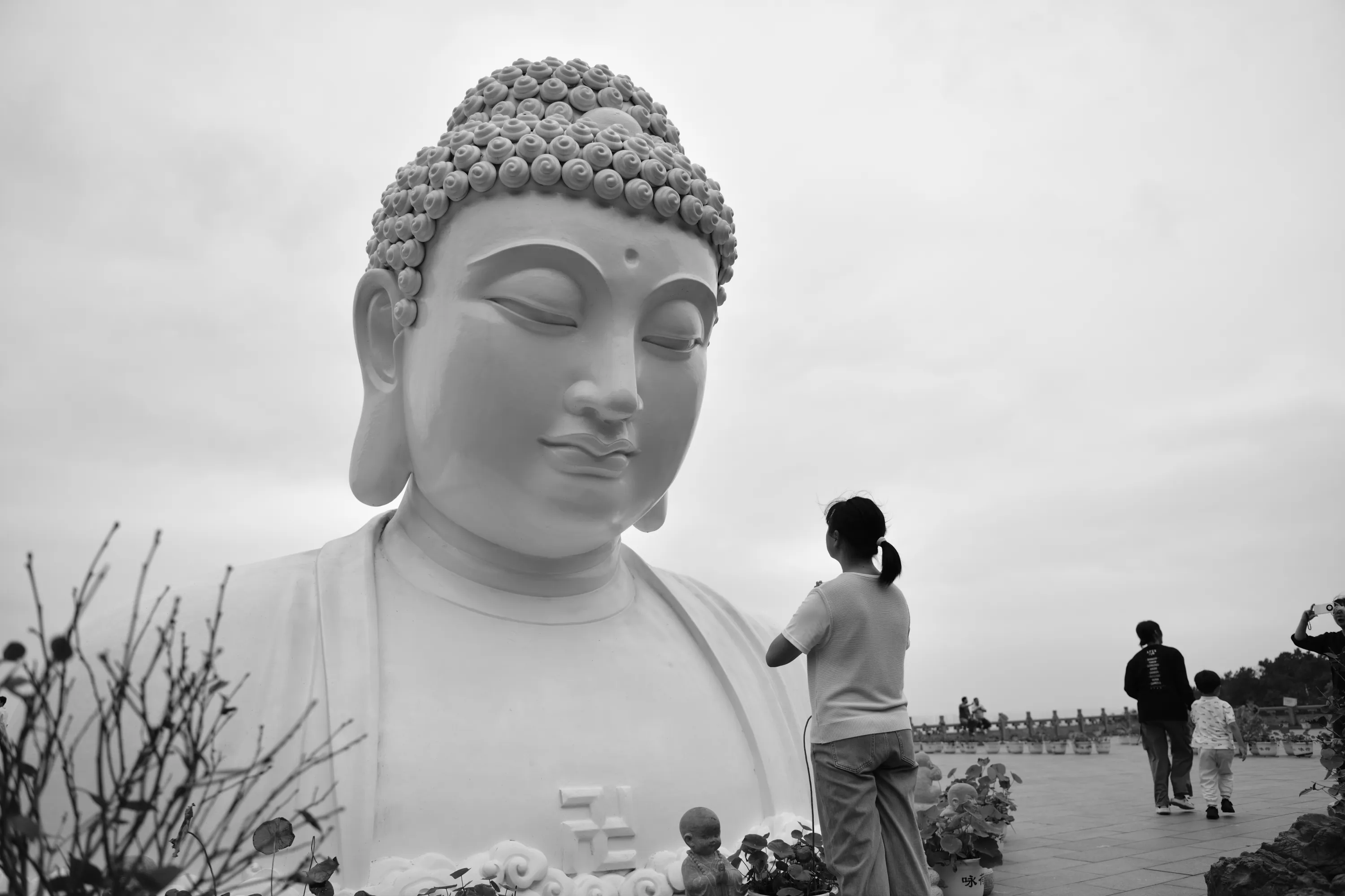 A white Buddha statue face beside visitors in a quiet outdoor setting
